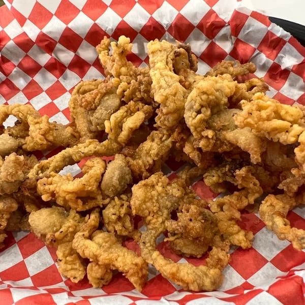 A close-up of crispy fried clams in a basket lined with red and white checkered paper.