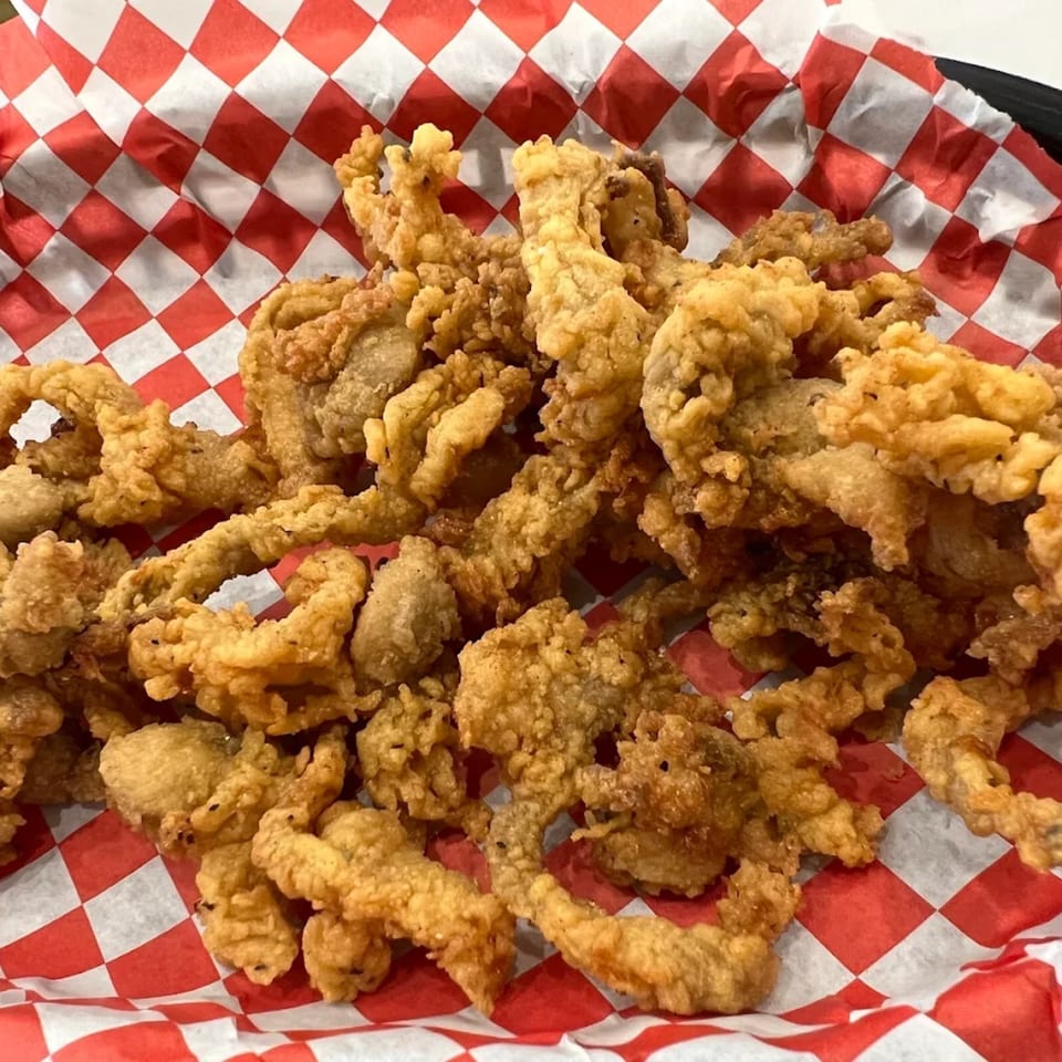 A close-up of crispy fried clams in a basket lined with red and white checkered paper.