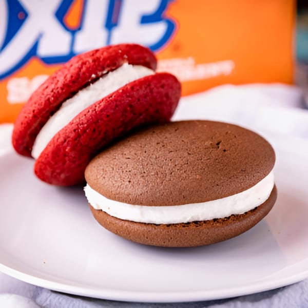 A red velvet whoopie pie and a chocolate whoopie pie with white cream filling on a white plate.